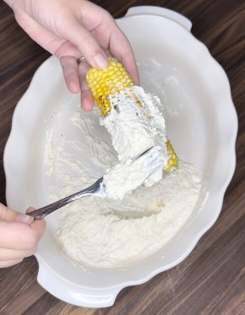 Applying coating of cream and seasonings on corn. 